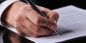 Dłoń trzymająca długopis, który podpisuje jakiś dokument